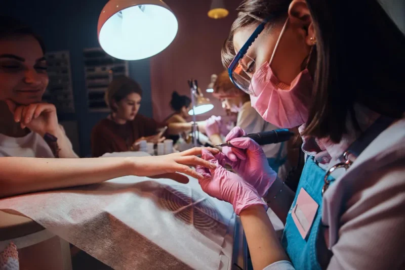 focused talented manicurist is working her own workplace busy beauty salon she is wearing protective mask